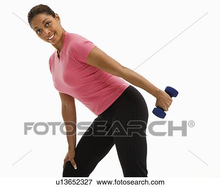 Stock Photo - Mid adult multiethnic woman exercising with dumbbell smiling and looking at viewer.. Fotosearch