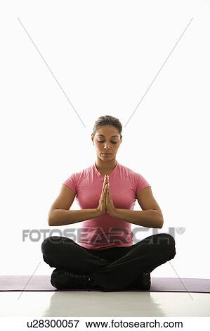 Stock Photo - Mid adult multiethnic woman sitting in Namaste position on exercise mat with eyes closed and hands at heart center.. Fotosearch