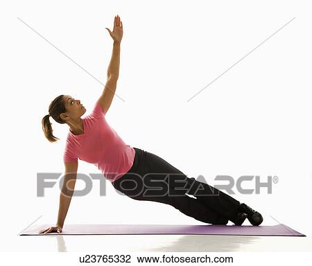 Stock Image - Mid adult multiethnic woman wearing exercise clothing holding yoga pose and stretching.. Fotosearch