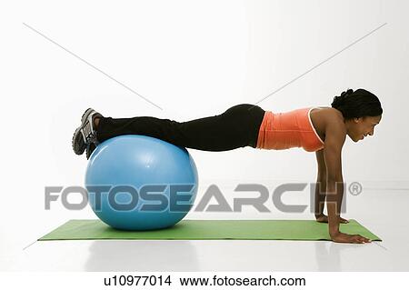 Picture - Profile of African American woman doing push ups with feet on exercise ball.. Fotosearch