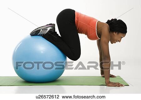 Stock Image - Profile of African American woman working out using an exercise ball.. Fotosearch