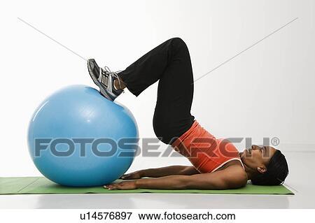 Stock Photo - Profile of African American woman stretching on mat with feet on exercise ball.. Fotosearch