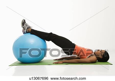Stock Photograph - Profile of African American woman stretching on mat with legs on exercise ball.. Fotosearch