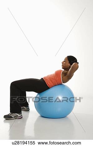 Stock Photography - Side view of African American woman balancing on exercise ball doing crunches.. Fotosearch