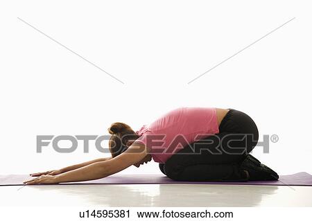 Stock Image - Side view of mid adult multiethnic woman wearing exercise clothing in childs yoga pose.. Fotosearch