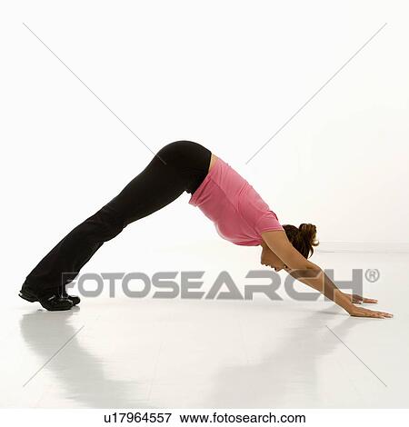 Stock Photo - Side view of mid adult multiethnic woman wearing exercise clothing in downward dog yoga pose.. Fotosearch