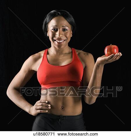 Smiling African American young adult woman holding apple with hand on hip. View Large Photo Image Stock Image - Smiling African American young adult woman holding apple with hand on hip.. Fotosearch