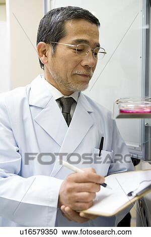 Stock Image - Mature scientist man writing a document in laboratory, side view. Fotosearch
