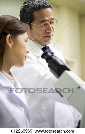 Stock Photo - Two scientists talking in laboratory, young woman in front of a microscope, side view. Fotosearch