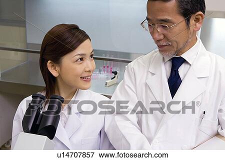 Two scientists talking in laboratory, young woman sitting in front of a Microscope, front view, high angle view View Large Photo Image Stock Photo - Two scientists talking in laboratory, young woman sitting in front of a Microscope, front view, high angle view. Fotosearch