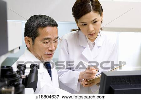 Two scientists talking in laboratory, young woman holding a document, side view, front view View Large Photo Image Stock Photo - Two scientists talking in laboratory, young woman holding a document, side view, front view. Fotosearch