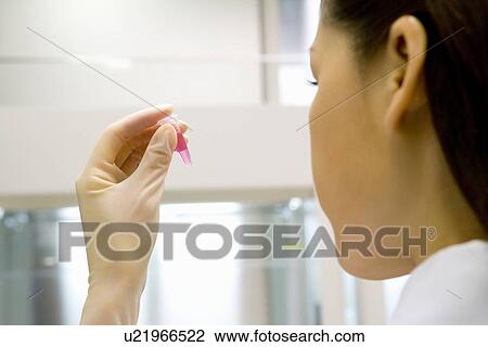 Stock Image - Young scientist woman looking at a test tube in laboratory, rear view, close up. Fotosearch