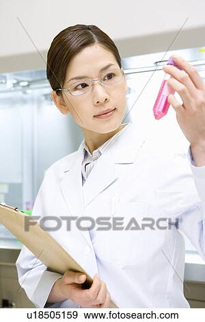 Stock Photo - Young scientist woman looking at a test tube and holding a document in laboratory, side view. Fotosearch
