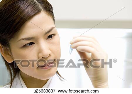 Stock Photo - Young scientist woman looking at a test tube in laboratory, front view. Fotosearch