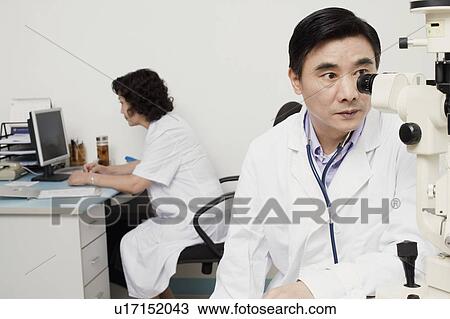 Stock Image - Close-up of an optometrist looking into an ophthalmoscope. Fotosearch