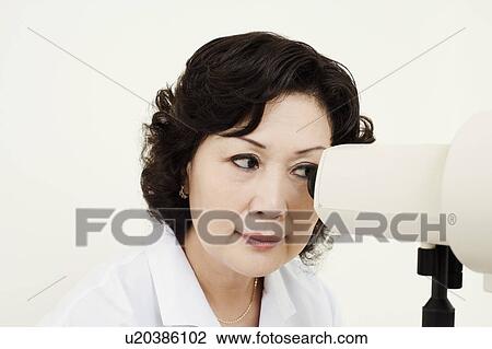 Stock Image - Close-up of an optometrist looking into an ophthalmoscope. Fotosearch