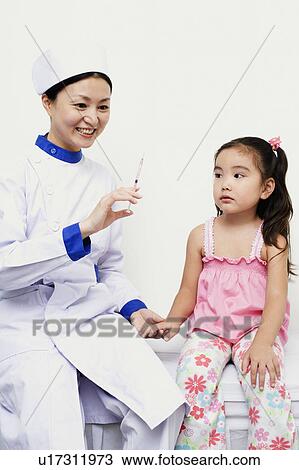 Stock Image - Female nurse holding a girl and a syringe. Fotosearch