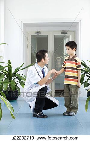 Male doctor crouching with a boy standing beside him View Large Photo Image Stock Photo - Male doctor crouching with a boy standing beside him. Fotosearch
