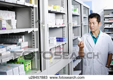 Male pharmacist looking at a bottle in a store room View Large Photo Image Stock Image - Male pharmacist looking at a bottle in a store room. Fotosearch