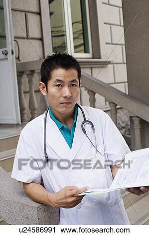 Stock Image - Portrait of a male doctor holding a report. Fotosearch