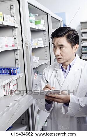 Stock Image - Male pharmacist writing in a store room. Fotosearch
