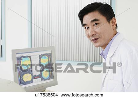 Picture - Portrait of a male doctor in front of a computer monitor. Fotosearch
