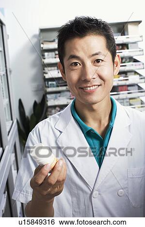 Stock Photograph - Portrait of a male pharmacist holding a bottle in a store room. Fotosearch