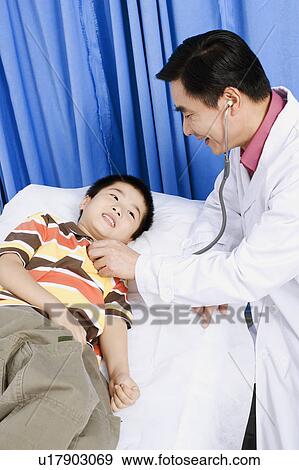 Stock Photo - Side profile of a male doctor examining a boy with a stethoscope. Fotosearch