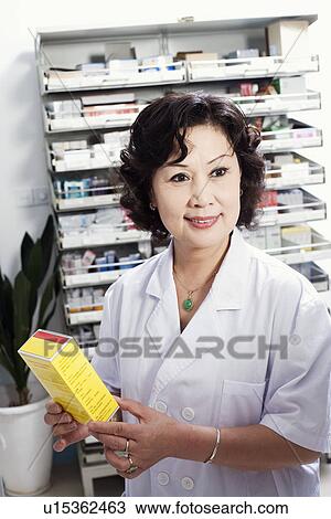 Stock Image - Close-up of a female pharmacist holding medicine in a store room. Fotosearch