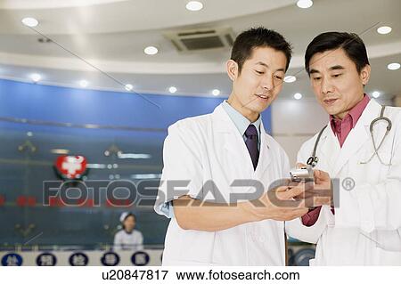 Stock Photo - Close-up of two male doctors looking at a personal data assistant. Fotosearch