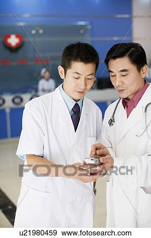 Stock Photo - Close-up of two male doctors looking at a personal data assistant. Fotosearch