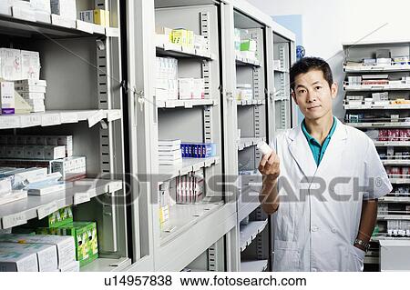 Portrait of a male pharmacist holding a bottle in a store room View Large Photo Image Stock Photo - Portrait of a male pharmacist holding a bottle in a store room. Fotosearch