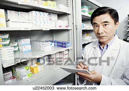 Stock Image - Portrait of a male pharmacist writing in a store room. Fotosearch