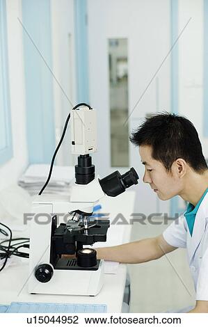 Stock Image - Side profile of a doctor looking into a microscope. Fotosearch