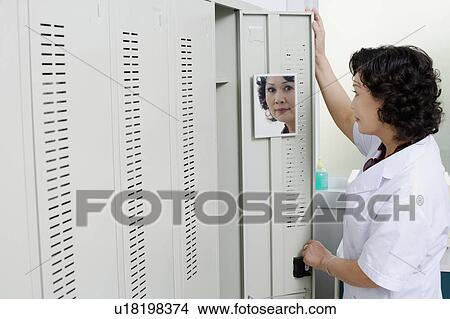 Side profile of a female looking at a mirror on the door of a locker View Large Photo Image Picture - Side profile of a female looking at a mirror on the door of a locker. Fotosearch