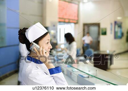 Stock Image - Side profile of a female nurse talking on the telephone. Fotosearch