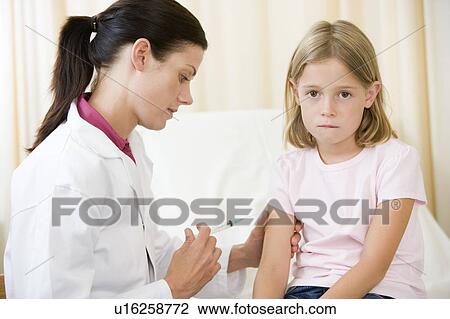 Stock Image - Doctor giving needle to young girl in exam room. Fotosearch