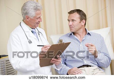 Picture - Doctor writing on clipboard while giving man checkup in exam room. Fotosearch