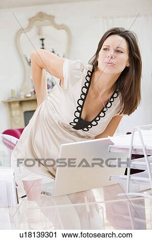 Stock Image - Pregnant woman in home office with a sore back. Fotosearch