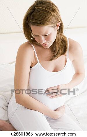 Stock Photography - Pregnant woman sitting in bed holding stomach in pain. Fotosearch