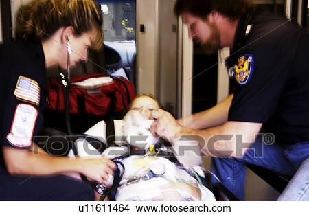 Picture - EMTs working on patient on stretcher. Fotosearch