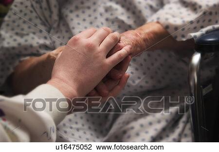 Stock Image - Senior woman in wheelchair holding hands with nurse. Fotosearch
