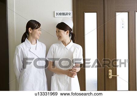 Stock Photo - Female nurse and doctor talking in front of door. Fotosearch