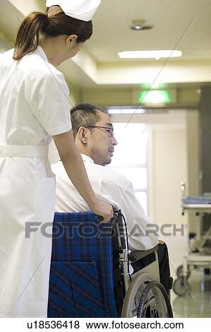 Stock Photo - Female nurse pushing a patient in wheelchair. Fotosearch
