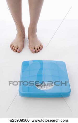 Stock Image - Woman standing next to bathroom scale. Fotosearch