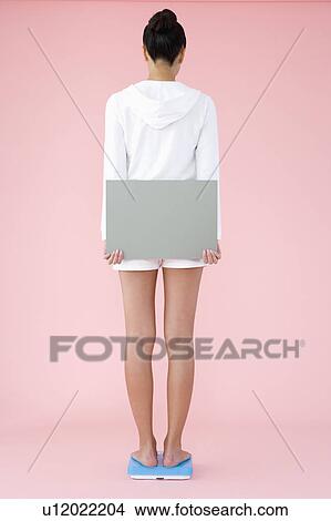 Picture - Woman standing on bathroom scale holding blank placard. Fotosearch