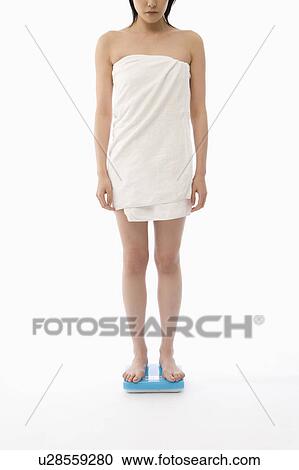 Stock Image - Woman standing on bathroom scale. Fotosearch