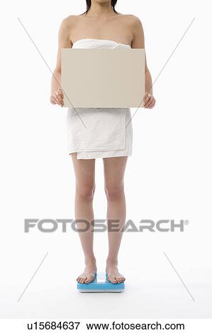 Stock Photo - Woman standing on bathroom scale holding blank placard. Fotosearch