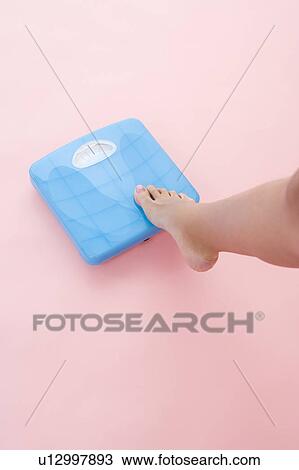 Stock Image - Woman stepping on bathroom scale. Fotosearch