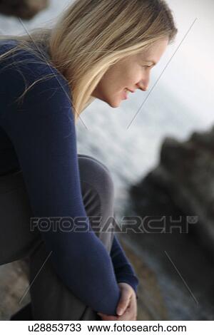Young blond woman sitting on a rock at the beach, side view View Large Photo Image Stock Image - Young blond woman sitting on a rock at the beach, side view. Fotosearch